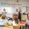 Classe de primaire avec des enseignantes et des élèves qui lèvent la main pour interragir en classe